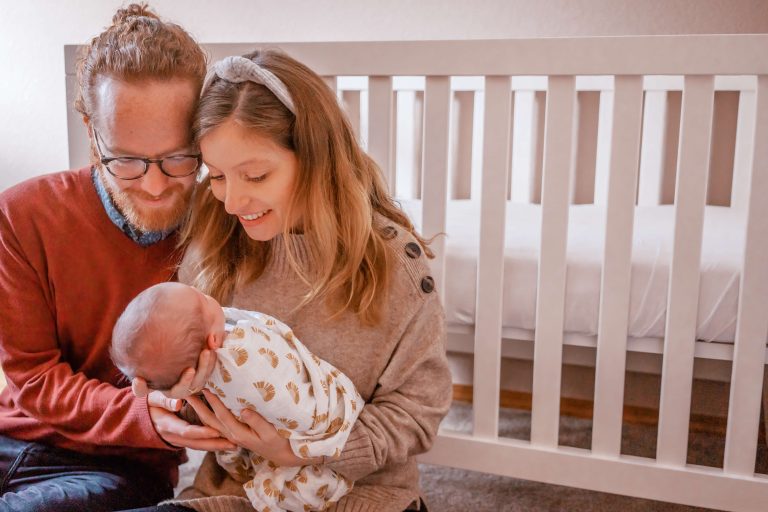 Couple holding their newborn baby in front of a crib